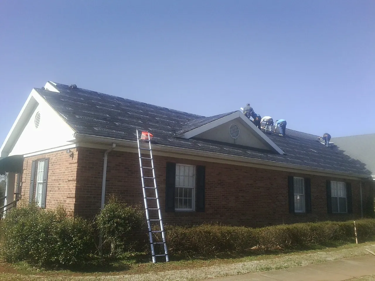 Crew tearing shingles off a brick ranch roof with a ladder set — Emergency Roof Repair work by our crew in Hasbrouck Heights