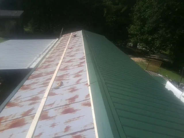 Old rusted panels beside newly installed green metal roofing — Wind Damage Roof Repair by Roofing Brothers in Hasbrouck Heights