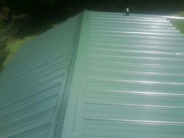 New green metal panels meeting at the ridge of a roof — Flat Roof Repair work by our crew in Hasbrouck Heights