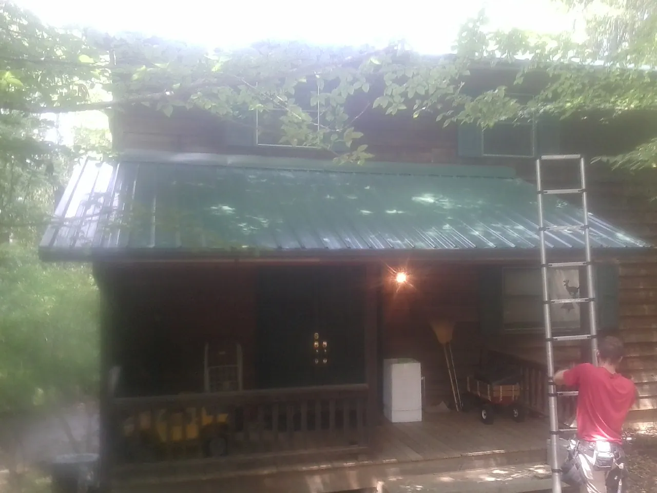 Worker on a ladder at the green porch roof of a wooded cabin in Hasbrouck Heights