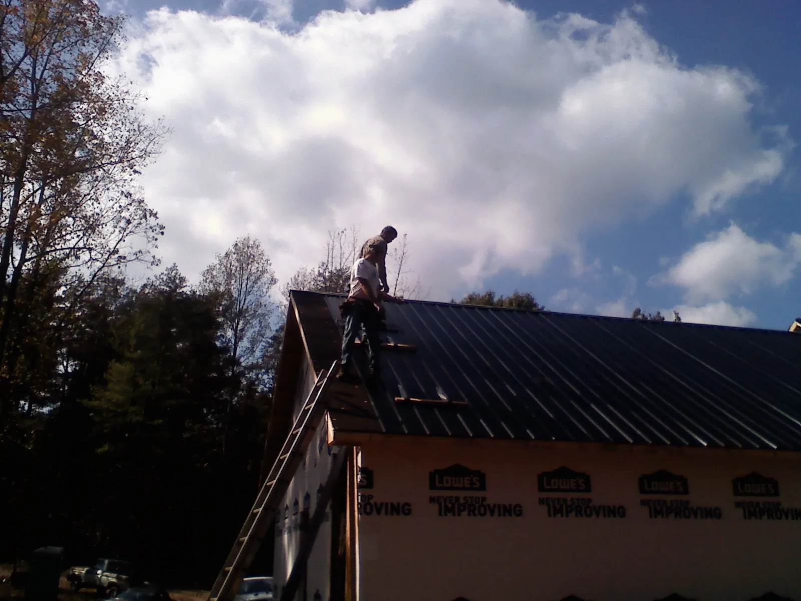Roofer fastening dark metal panels high against a cloudy sky, from a Roof Inspection job in Hasbrouck Heights