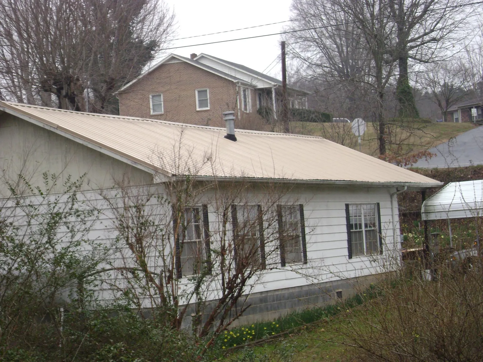 Tan metal roof on a white sided house set into a hillside — Commercial Roofing by Roofing Brothers in Hasbrouck Heights